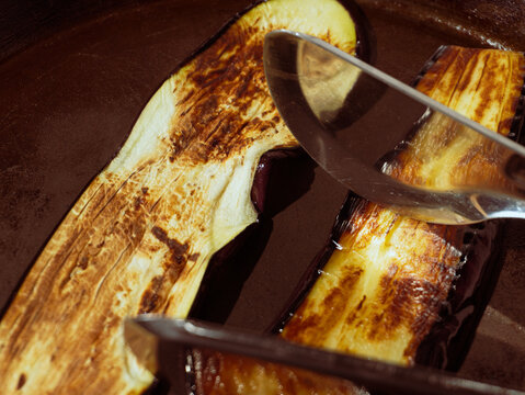 Fried eggplant slices being flipped with metal tongs in a frying pan
