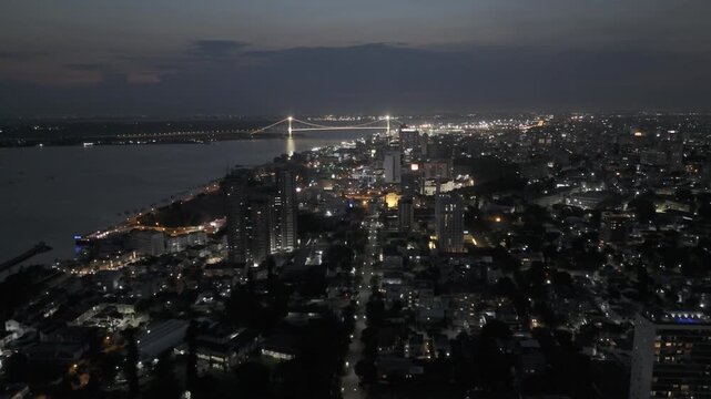 Drone flies backwards over Polana Cimento A with view of city and suspension bridge crossing the Mbuluzi River at night in Maputo, Mozambique