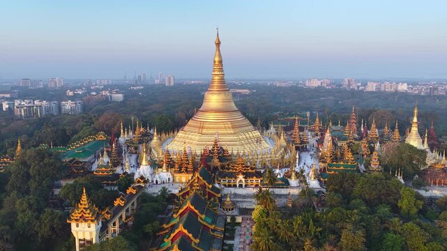 Aerial drone view at Shwedagon Pagoda, a golden stupa, surrounded by lush greenery and urban development in Yangon (Rangun), Myanmar (Burma), showcasing the city's blend of religious and modern life.
