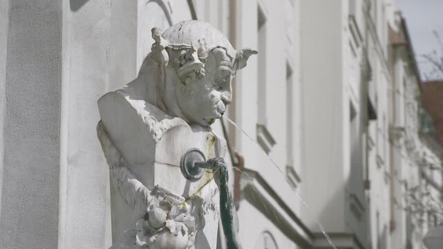 Water flowing from the mouth of a grotesque gargoyle statue on a historic building facade