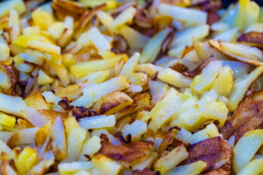 Detailed macro view displays various golden brown crispy potato batons sizzling alongside soft translucent onion pieces creating textured savory dish during pan frying process