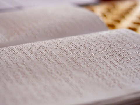 Close up view of white paper pages featuring raised tactile dots forming braille alphabet text for finger reading by people with visual disabilities