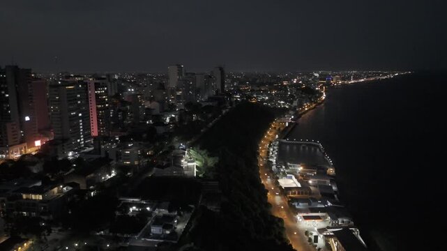 Drone facing north lowers over Jardim dos Namorados at night with the coastal highway lit up in Maputo, Mozambique