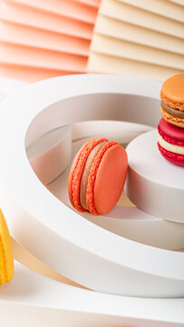 Vibrant macarons in various colors are beautifully arranged on a sleek white display, surrounded by soft pastel textures and shapes, phone background with copy space