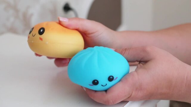 two hands holding and squeezing blue and yellow kawaii antistress squishy dumpling toys with cute smiley faces close-up horizontal