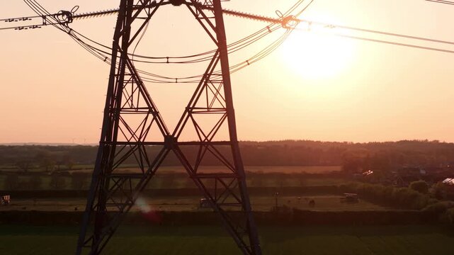 Aerial view of a high-voltage electricity pylon silhouette against a golden sunset over fields and houses in Armthorpe, Doncaster, England, United Kingdom.