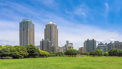 青空の下に広がる都会の公園の芝生広場と高層マンション群の景観  © 茂明 北村