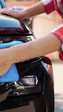 Young woman in shorts wipes a car with a rag at a self service car wash