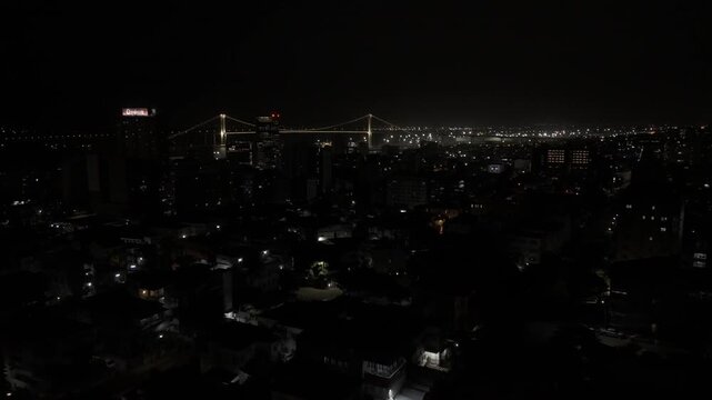 Drone flies northwest over city toward suspension bridge lit up over the Mbuluzi River at night in Maputo, Mozambique