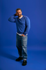 Naklejka premium Stylish man with a charming smile poses against a vibrant blue background in modern attire