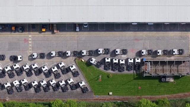 Aerial view of rows of white truck cabs parked outside a large logistics warehouse with green grass and asphalt in Doncaster, England, United Kingdom.