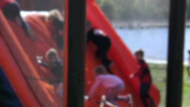 Group of unrecognizable blurred children having fun and playing while climbing a large inflatable attraction in a park on a sunny day, showcasing childhood joy and outdoor recreation