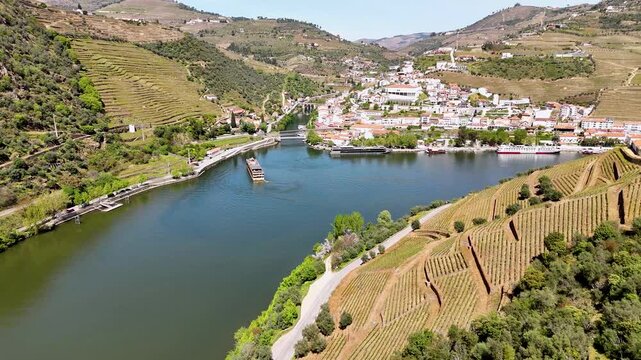Aerial view of the Douro River flowing past the town of Pinhao and lush terraced vineyards under a clear sky in Pinhao, Vila Real, Portugal.