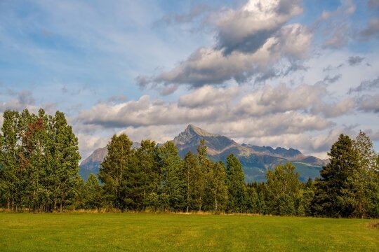 Scenic view of Krivan peak in the High Tatras, Slovakia, surrounded by forest and green meadow under dramatic clouds. Iconic Slovak mountain landscape in warm natural light.