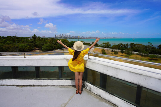 Visiting Joao Pessoa, Paraiba, Brazil. Back view of young woman with open arms on Estacao Cabo Branco viewpoint, Joao Pessoa, Brazil.
