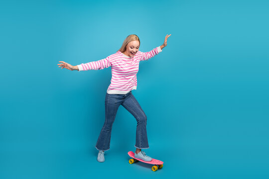 Woman balancing on a pink skateboard against a bright blue background, laughing and enjoying a playful active lifestyle