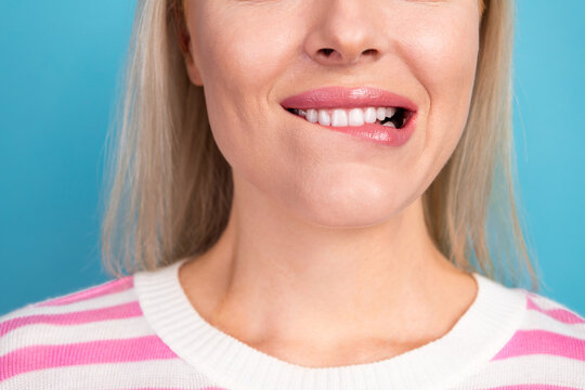 Young woman biting her lip with a playful, nervous smile in a striped sweater against a blue background