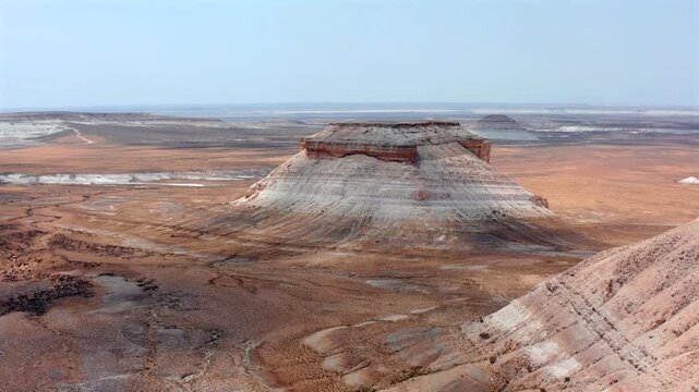 Drone flies forward toward isolated chalk mesa in Bozzhyra Mangistau Kazakhstan revealing layered limestone slopes, erosion patterns and vast arid plateau with dramatic natural landforms
