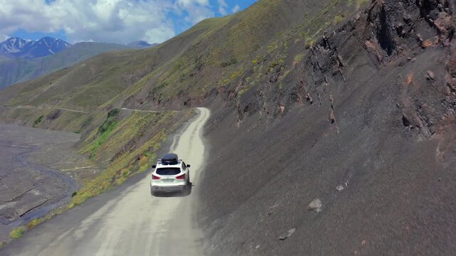 Aerial drone shot of SUV driving along winding serpentine mountain road in Azerbaijan, showing sharp switchbacks, steep hillside terrain and scenic remote travel landscape