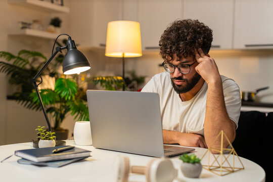 Arabian man at home ends remote laptop job feels bored tired stress burnout wants rest. Egyptian guy sitting at table rubs face sighs low energy looks aside plans pause from tasks tonight.