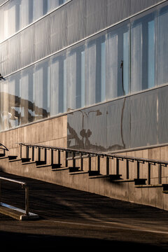 Long ramp and handrail guide perspective as modern minimal architecture building windows and lines sit in shadow with clear foreground space