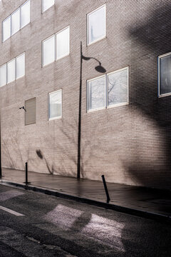 Hard sunlight hits a brick wall as architecture windows and facade shape an urban street with minimal shadow and clean foreground space