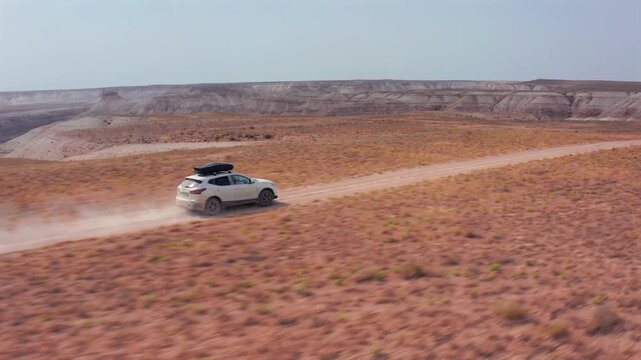Aerial follow shot of SUV driving along winding dirt road through Bozzhyra desert in Mangistau Kazakhstan, showing remote landscape, travel route and offroad journey across vast arid terrain