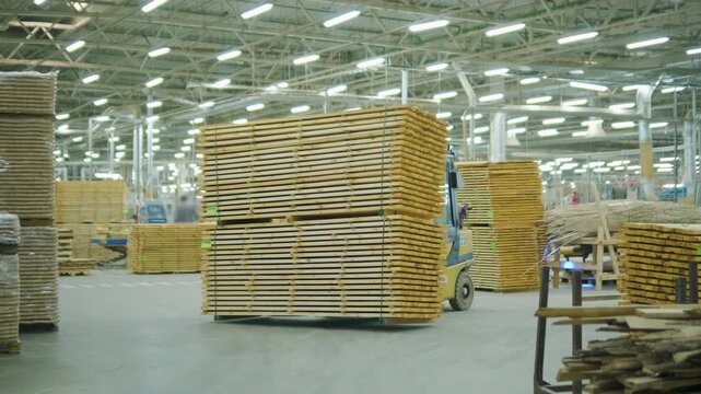 A large industrial warehouse featuring a forklift operating among stacks of dried wooden planks prepared for further furniture or flooring production