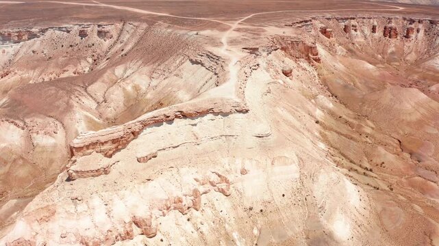Drone captures elevated view of eroded ridge and canyon cut in Bozzhyra Mangistau Kazakhstan showing chalk and limestone layers, natural erosion channels and dry desert terrain patterns