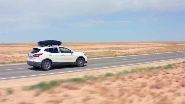 aerial camera tracking car moving left to right side view along straight asphalt road in Mangystau Kazakhstan, smooth motion across flat desert terrain showing constant speed and long distance travel