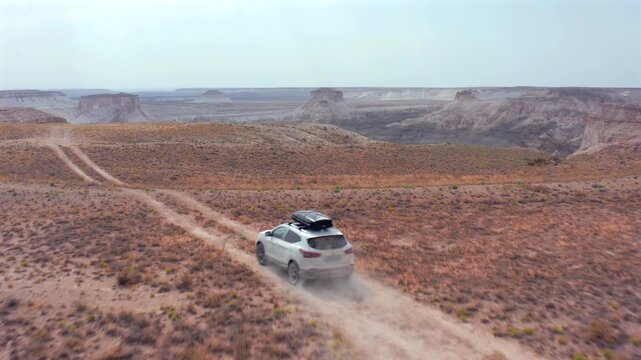 Aerial drone shot of SUV with roof box driving along one of several dirt tracks across Bozzhyra desert in Mangistau Kazakhstan, with branching routes through ancient seabed formations