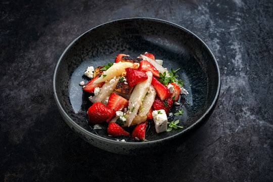 Fresh made spring mixed salad with white asparagus, strawberries, feta sheep cheese and roasted sweet bread croutons served as close-up in a design bowl