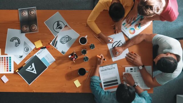 Top view of designer writing and designing logo graphic at meeting. Closeup of business man working on colored palettes and writing idea on sticky notes on table with equipment and paper. Symposium.