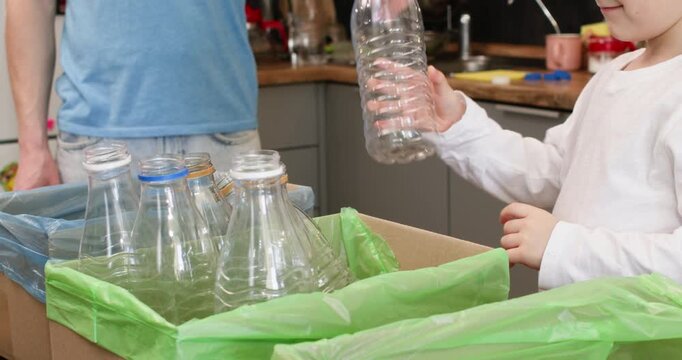 Boy arranges clear plastic bottles inside green recycling box at home. Child preschooler sets container in row continuing sorting with steady hands and focus in kitchen