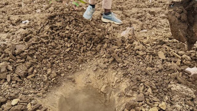 Close view of auger drill bit coming out of ground with soil falling off spiral blades, showing completed drilling process in a rural agricultural setting