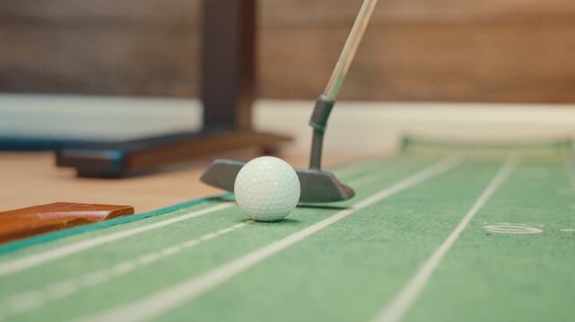 Slow motion close up of a putter striking golf ball on an indoor training mat. Golf training videos, putting drill, practice, and product ads.