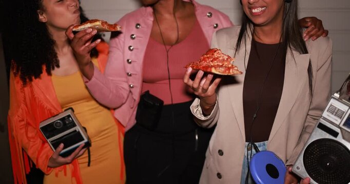 Group of multiracial girls having fun eating pizza together while listening music with vintage retro devices outdoor - Party, nightlife and people lifestyle concept 