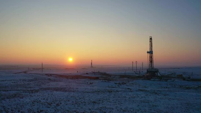 Oil drilling rig at sunset across snowy gas field landscape.
