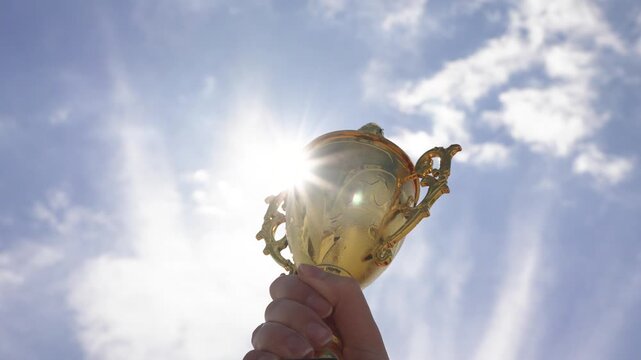 Close-up of a hand holding a trophy against sky background outdoors. Concept of achievement, success, victory, motivation, recognition, and celebration of winning moment.