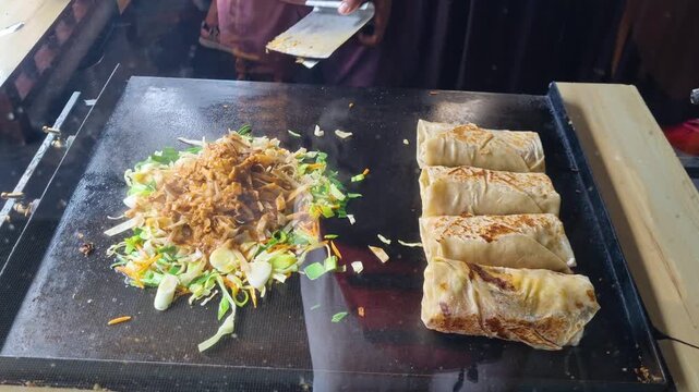 Street vendor in Ella, Sri Lanka rapidly slicing and tossing roti on a sizzling metal plate, combining egg, vegetables, and curry into the iconic Kottu Roti in a lively cooking performance