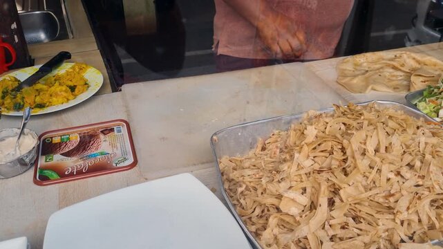 Local cook skillfully rolls spiced vegetable curry into flatbread to make Kottu roti wraps in Ella, Sri Lanka, with chopped roti strips prepared for the next batch of this popular street food