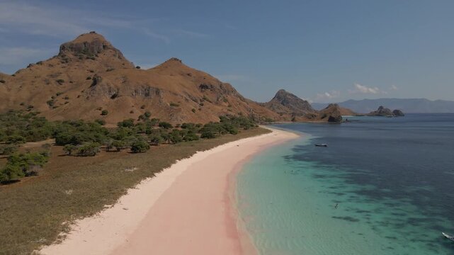 Drone pullout from rare pink sand beach on Padar Island Komodo revealing turquoise blue sea and dramatic volcanic mountain backdrop Indonesia