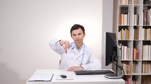 Doctor sitting at desk in white lab coat and stethoscope, expressing dissatisfaction and disapproval with a negative thumbs down gesture at the camera
