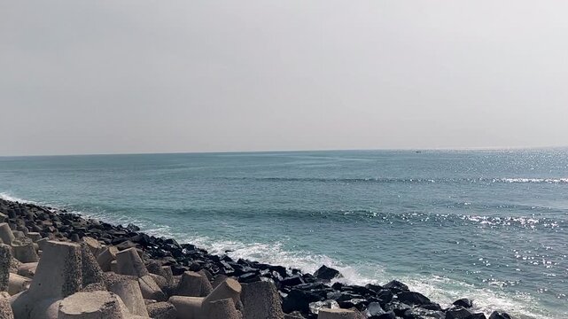 Waves hitting coastal breakwater with tetrapods and rocks under clear sky. Ideal for coastal engineering, sea defense, travel visuals, and calm seaside backgrounds.