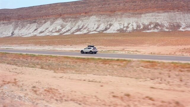 aerial camera tracking small car driving sideways far view along asphalt road near white limestone ridge in Mangystau Kazakhstan, lateral motion across desert terrain emphasizing distance and scale