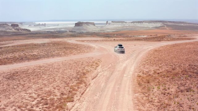 aerial camera tracking car driving away rear view toward forked dirt junction in Bozzhyra tract Mangystau Kazakhstan, forward motion across dry canyon plains showing route choice, remote exploration