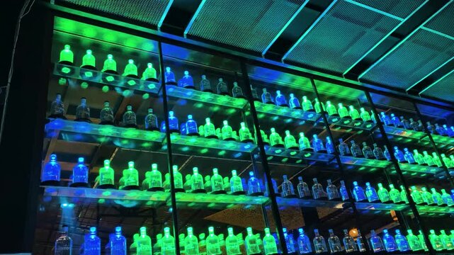 illuminated liquor bottle display wall with neon blue and green lights inside modern nightclub bar