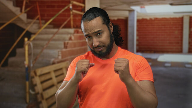 Man clenches fists and looks down inside a building under construction with bare forearms visible and tense expression; frustration resilience.