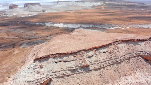 Drone glides along chalk cliff edge in Bozzhyra Mangistau Kazakhstan exposing horizontal limestone layers, erosion textures and vast desert plateau stretching to distant horizon