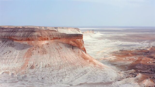 Aerial view of dramatic layered canyon cliffs and white desert formations in Bozzhyra Mangistau Kazakhstan, showcasing erosion patterns, geological structure and vast natural landscape textures